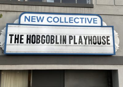 Art Deco-style light-up marquee with blue trim and silver accents that says "New Collective" in large blue block letters, and "The Hobgoblin Playhouse" in larger black letters beneath.